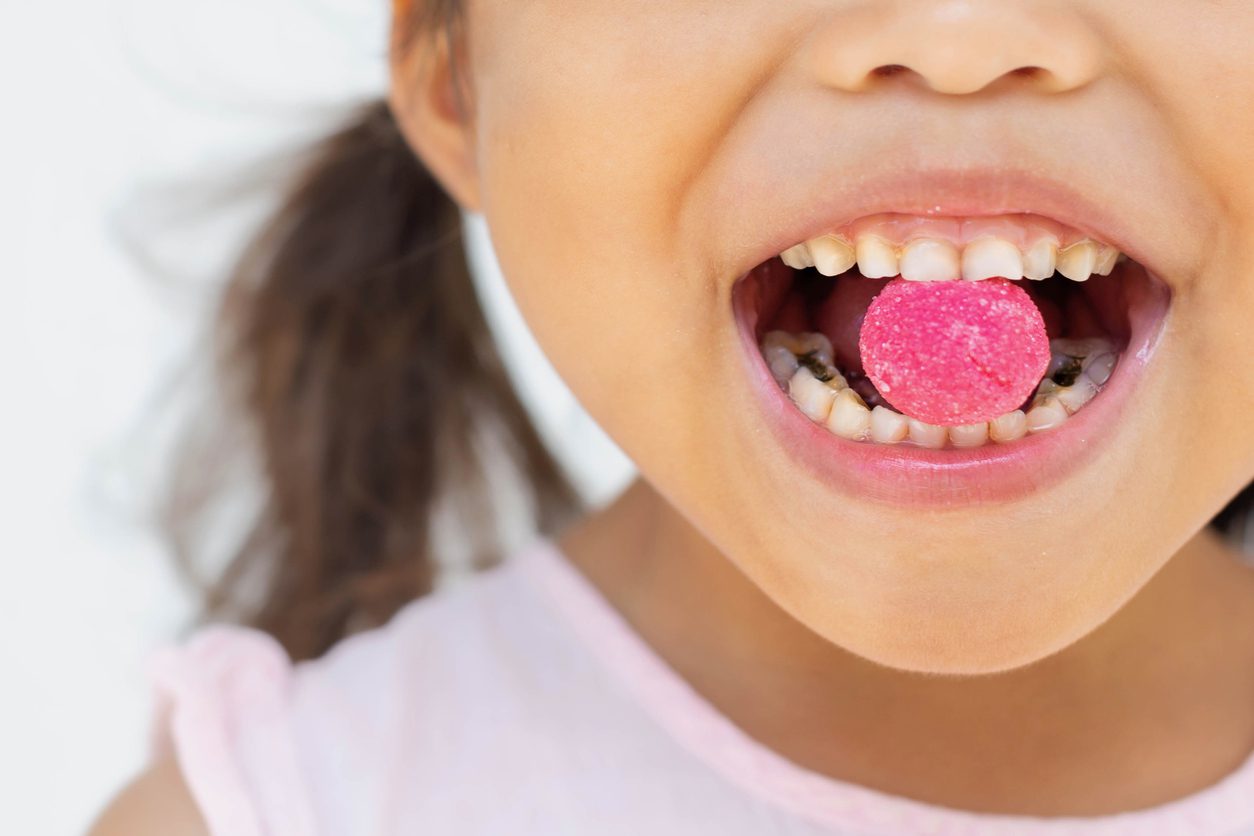 A little girl with a pink piece of sugar candy in between her teeth