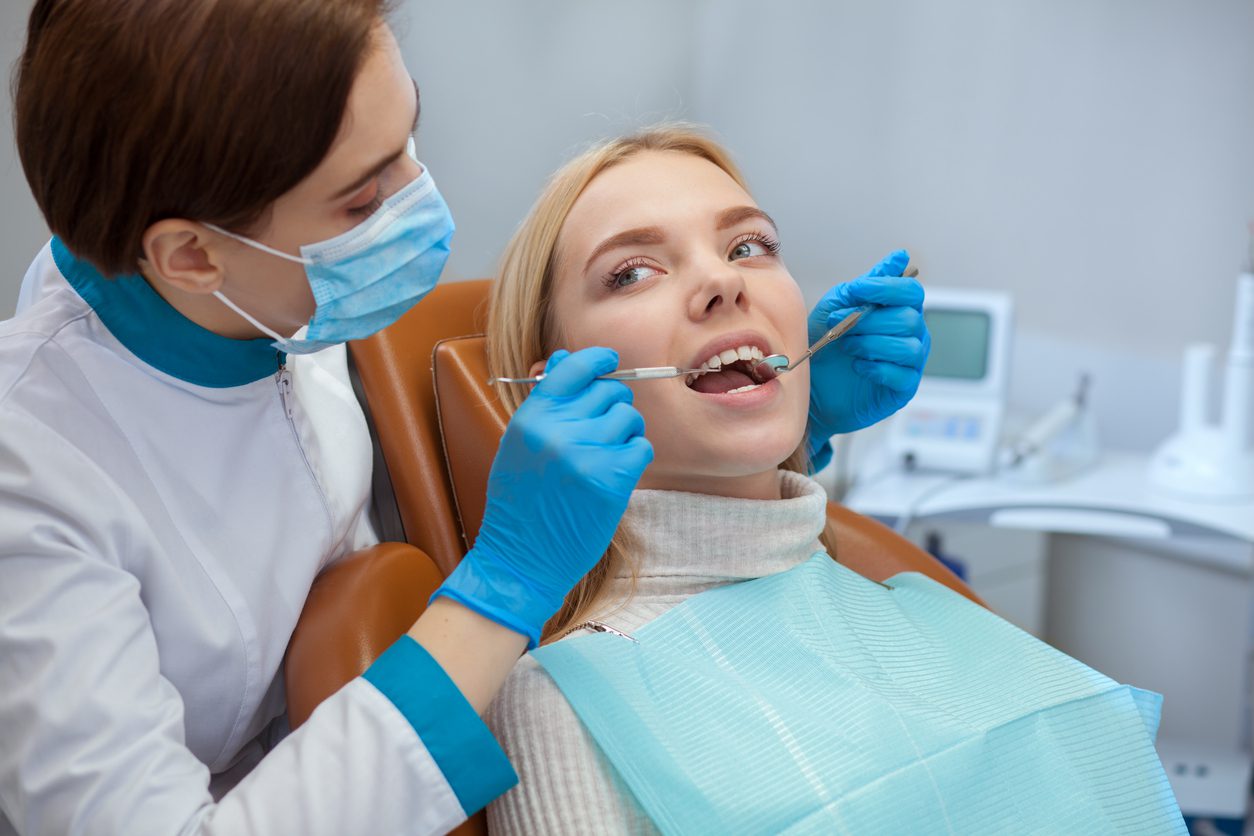 Professional dentist wearing medical mask, examining teeth of a female patient,